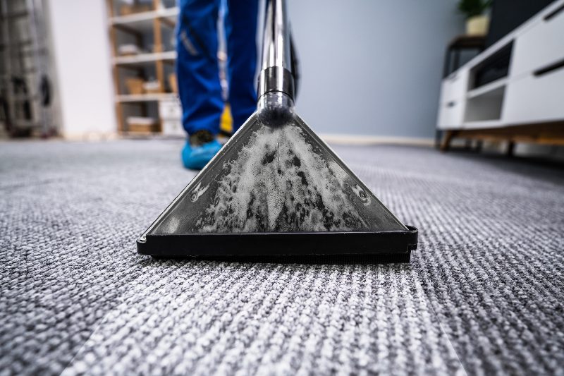A technician running a carpet cleaning wand over commercial carpet