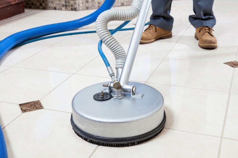 A rotary tile and grout cleaning tool at work on a tiled floor
